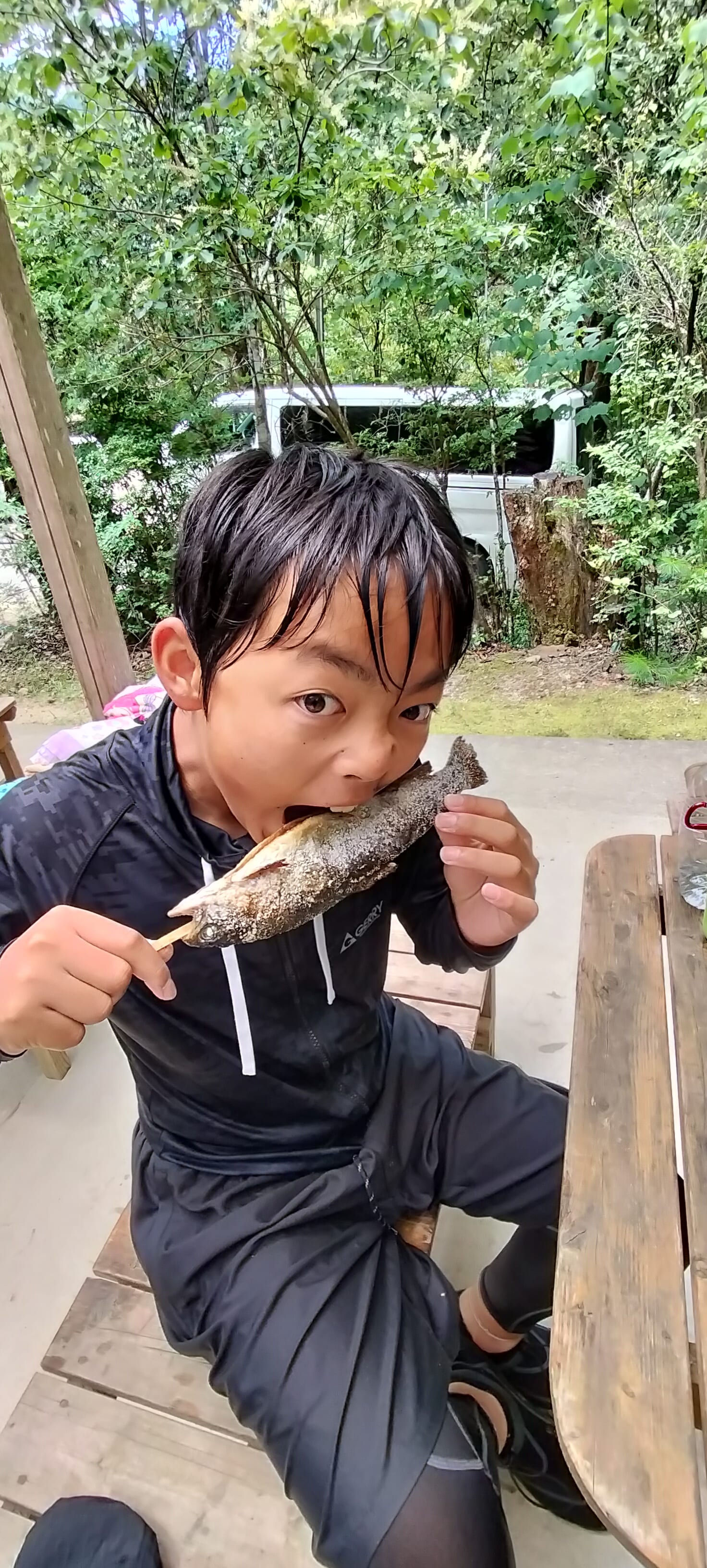 串に刺したニジマスの塩焼きにかぶりつく